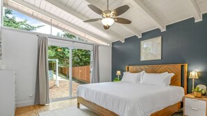 Una camera da letto con un letto grande, una ventola a soffitto, un comodino e vista su uno spazio esterno attraverso una porta scorrevole in vetro.