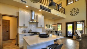 A spacious kitchen with a large island, white cabinetry, and a hanging light fixture.