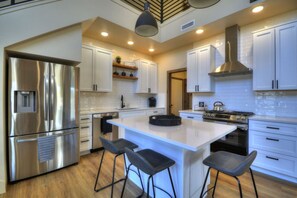 A modern kitchen with white cabinets, stainless steel appliances, a central island with bar stools, and a pendant light. - Summit Sky Retreat, Red Lodge (Red Lodge)