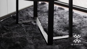 A round table with a white cup and saucer, a potted plant, and a magazine on a black furry rug. - NB APARTMENT - KIM MA (Hanoi)