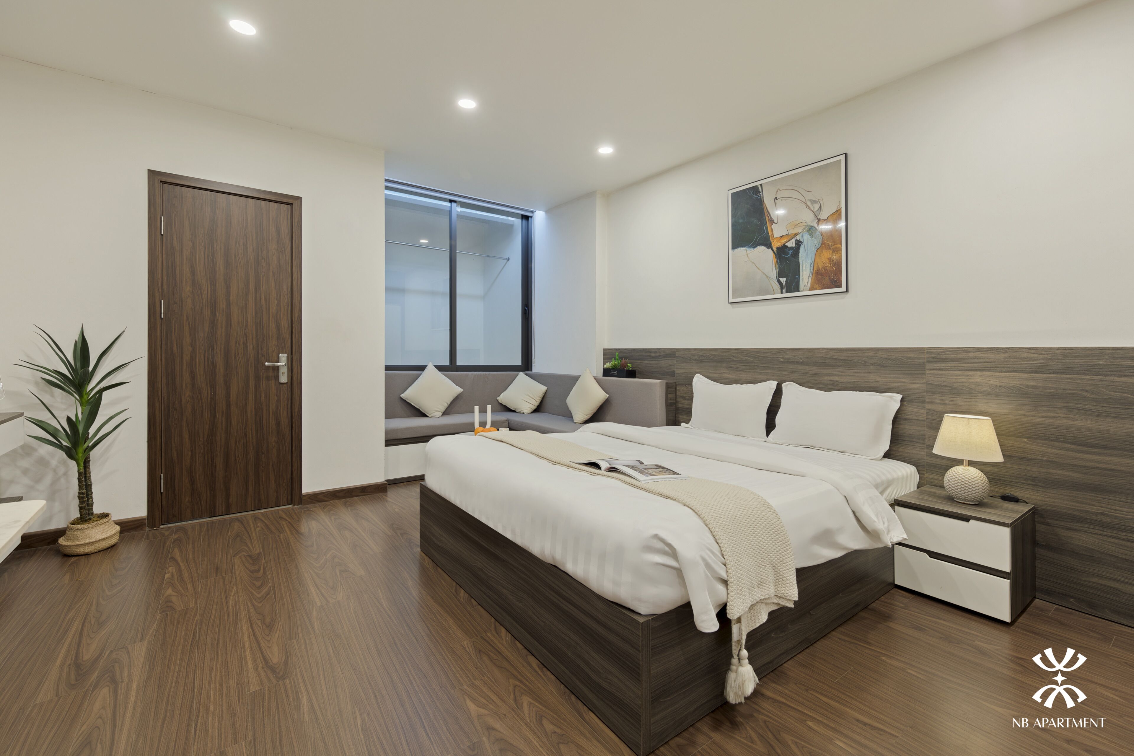 Une chambre moderne avec un grand lit, des tables de chevet, une petite table, une plante en pot et une fenêtre donnant sur un beau paysage.