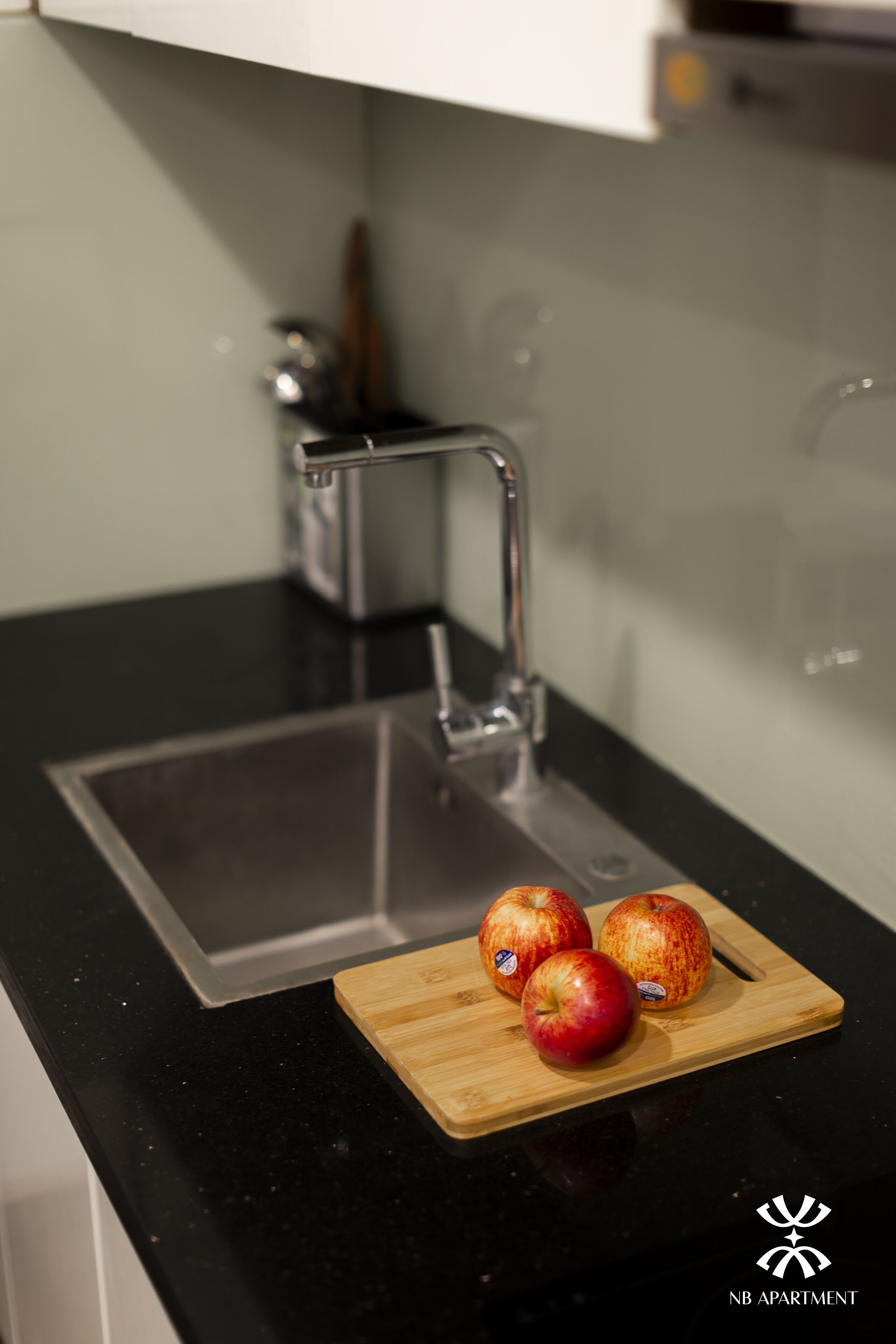 A kitchen counter with a cutting board holding three apples and a stainless steel faucet.
