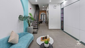 A modern apartment interior with a staircase, a blue sofa, a coffee table with a plant, and a kitchen area with cabinets. - NB APARTMENT - KIM MA (Hanoi)