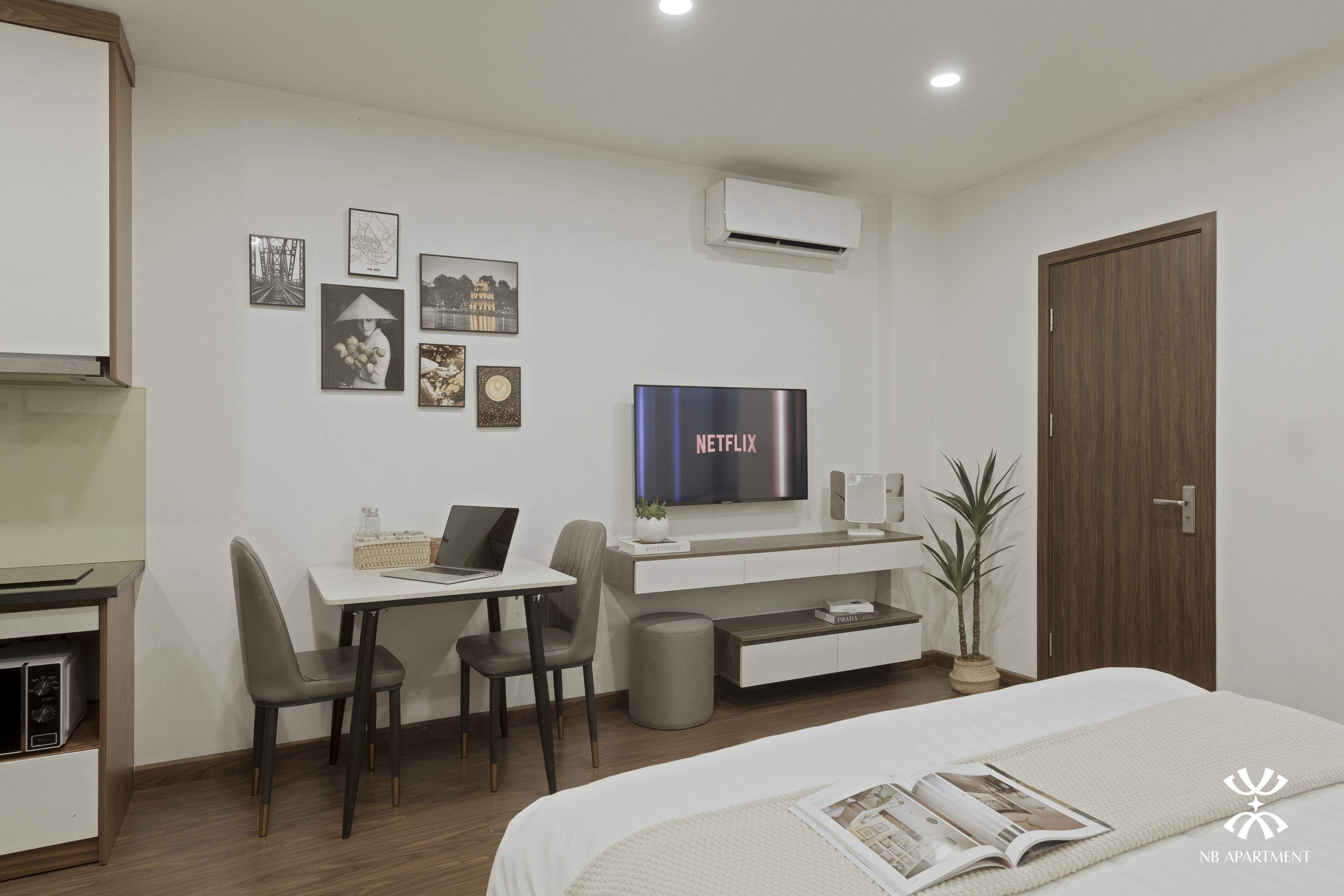 A modern hotel room with a bed, a desk with a laptop, a TV, and a small potted plant.