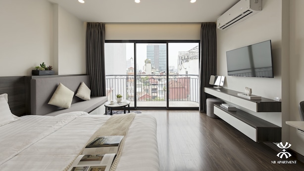 A modern hotel room with a large bed, a TV, a balcony with a city view, and a desk with a chair. - NB APARTMENT - KIM MA (Hanoi)