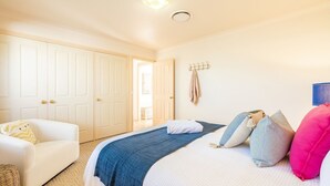 Un dormitorio con una cama, una silla blanca, un armario y un perchero en la pared.