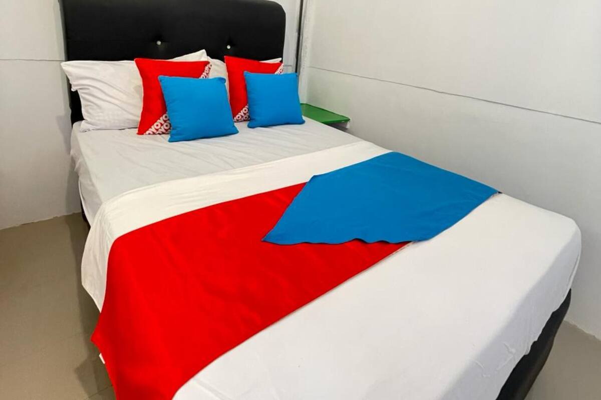 A neatly made bed with white bedding, red and blue pillows, and a red and blue blanket.