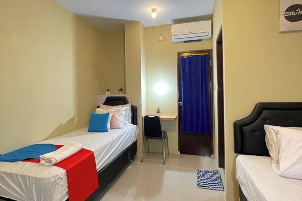 A hotel room with two beds, a desk, and an air conditioning unit.