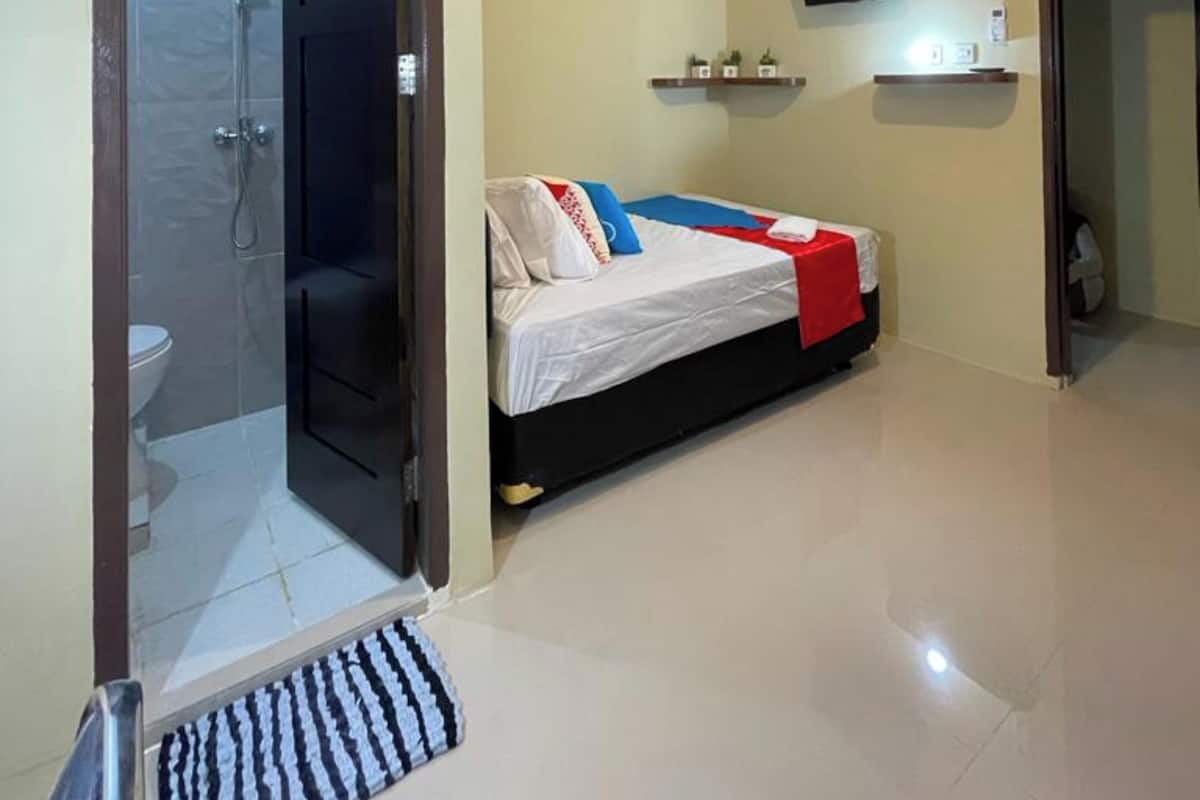 A modern bedroom with a bed, a TV mounted on the wall, and a shower area visible through an open door.