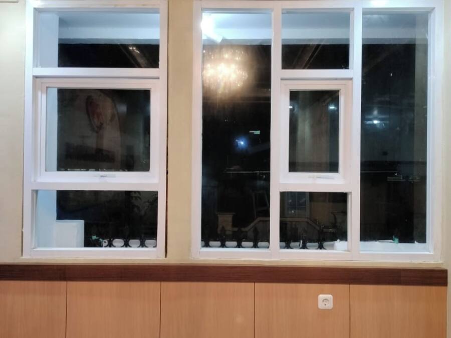 A room with a wooden panel baseboard, two windows with white frames, and a visible electrical outlet.