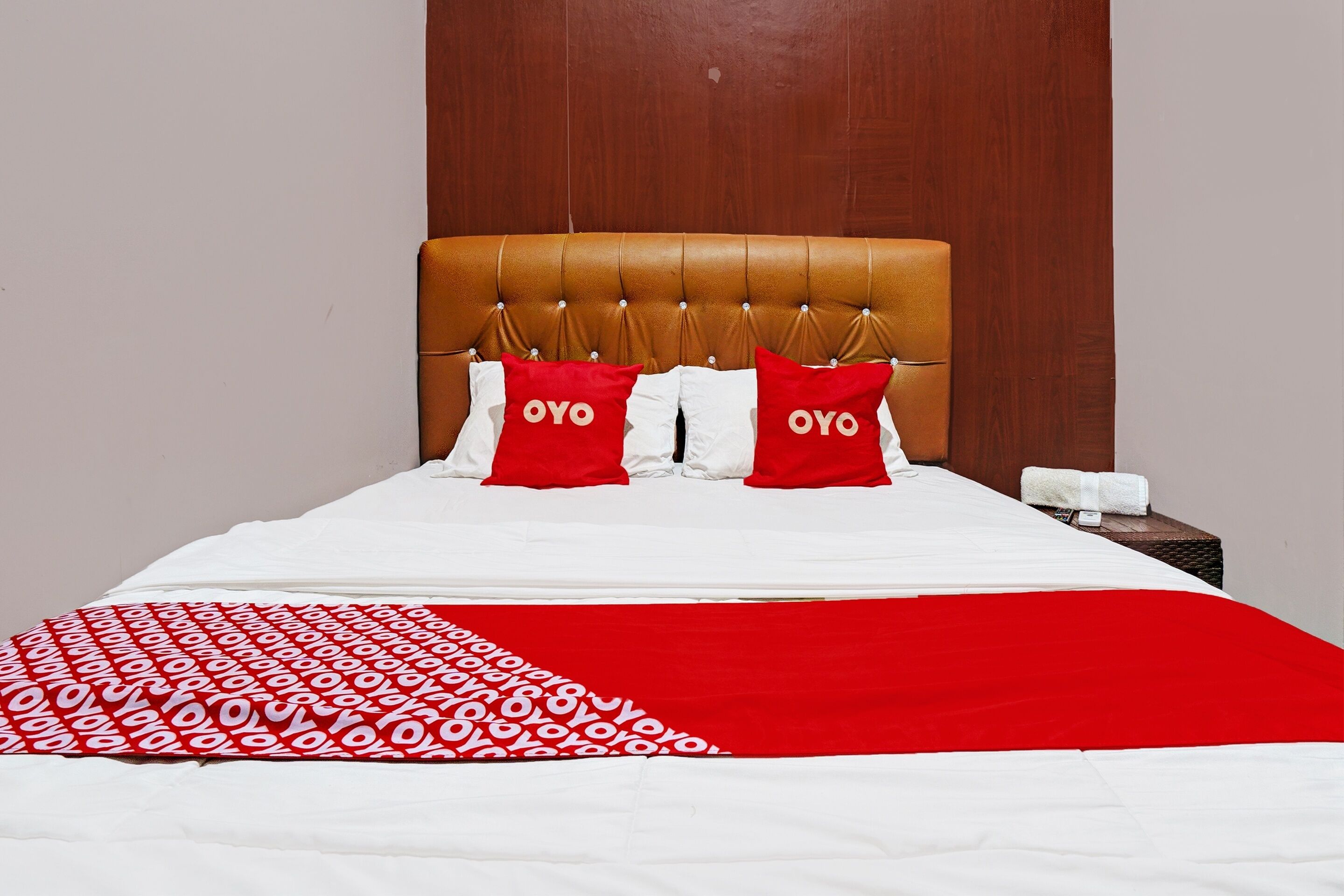 A neatly made bed with a red and white patterned blanket, two red pillows with the word "OYO" on them, and a wooden headboard.