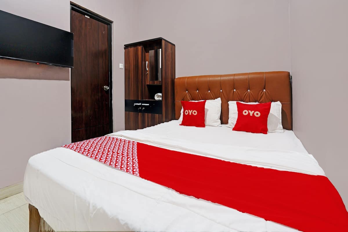 A neatly made bed with a red and white bedspread, a brown upholstered headboard, and two pillows with the word "OYO" on them.