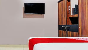 Una habitación con una cama, un televisor montado en la pared y un armario de madera con espejo.