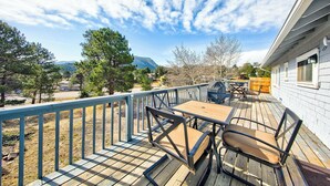 Une terrasse en bois avec une table et des chaises, un barbecue et une vue sur une montagne et des maisons au loin.