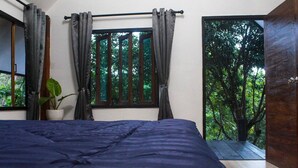Un dormitorio con cama, ventana con cortinas, una planta en maceta y vista a áreas verdes.