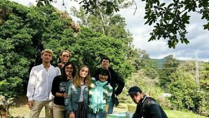 Un grupo de personas al aire libre junto a una mesa cubierta con un mantel verde.