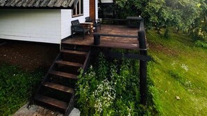 Una casa rústica con una terraza de madera, una escalera que lleva a la entrada y exuberante vegetación a su alrededor.