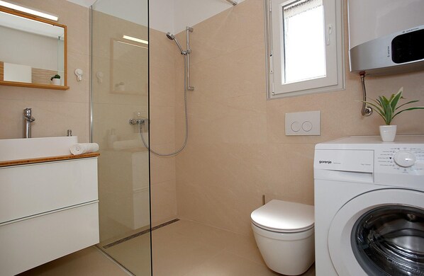 Un baño moderno con ducha de vidrio, inodoro, lavadora y lavabo con espejo.