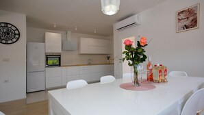 A modern kitchen with white cabinets, a built-in oven, and a dining area with a white table and chairs. - Luxurious home in Nin (Nin)