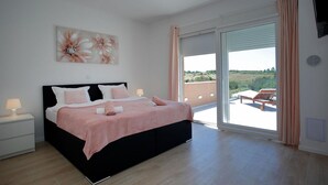 A bedroom with a black bed, white pillows, a pink bedspread, and a large window with a view of a balcony. - Luxurious home in Nin (Nin)