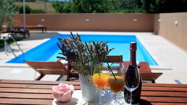A poolside setting with a wooden table, a rose, a vase with lavender, two glasses of orange juice, and a bottle of wine. - Luxurious home in Nin (Nin)