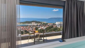Un balcon avec une table et des chaises, donnant sur une ville côtière avec ses bâtiments et offrant une vue sur la mer.