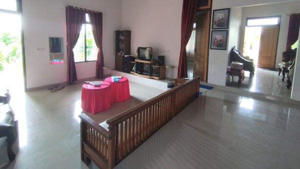 A spacious living room with a wooden bench, a television, and a dining area with a red table. - Hotel O Excellent Kost (Jambi)