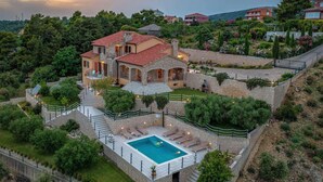 Una amplia casa de piedra con piscina, rodeada de abundante vegetación y un jardín cuidado.