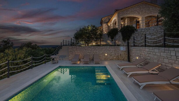 Un edificio de piedra con piscina y sillas de descanso.