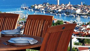 Una mesa de madera con platos y cubiertos, con vistas a un puerto deportivo con barcos y una ciudad costera.