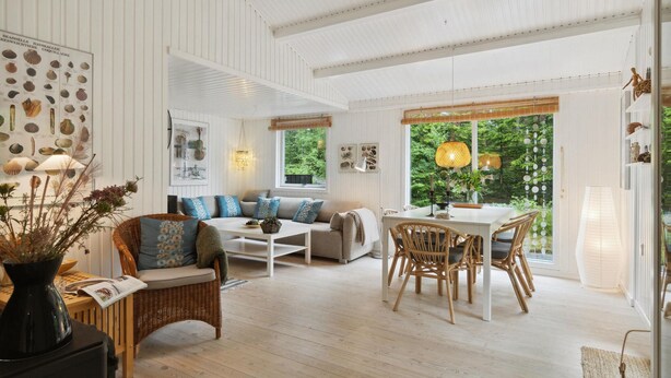 A spacious living room with a high ceiling, a dining area with wicker chairs, and a large window offering a view of greenery. - Nice home in ålbæk with WiFi (Ålbæk)