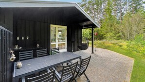 A wooden cabin with a dining area featuring a table and chairs, a hanging chair, and a door with glass panels. - Nice home in ålbæk with WiFi (Ålbæk)