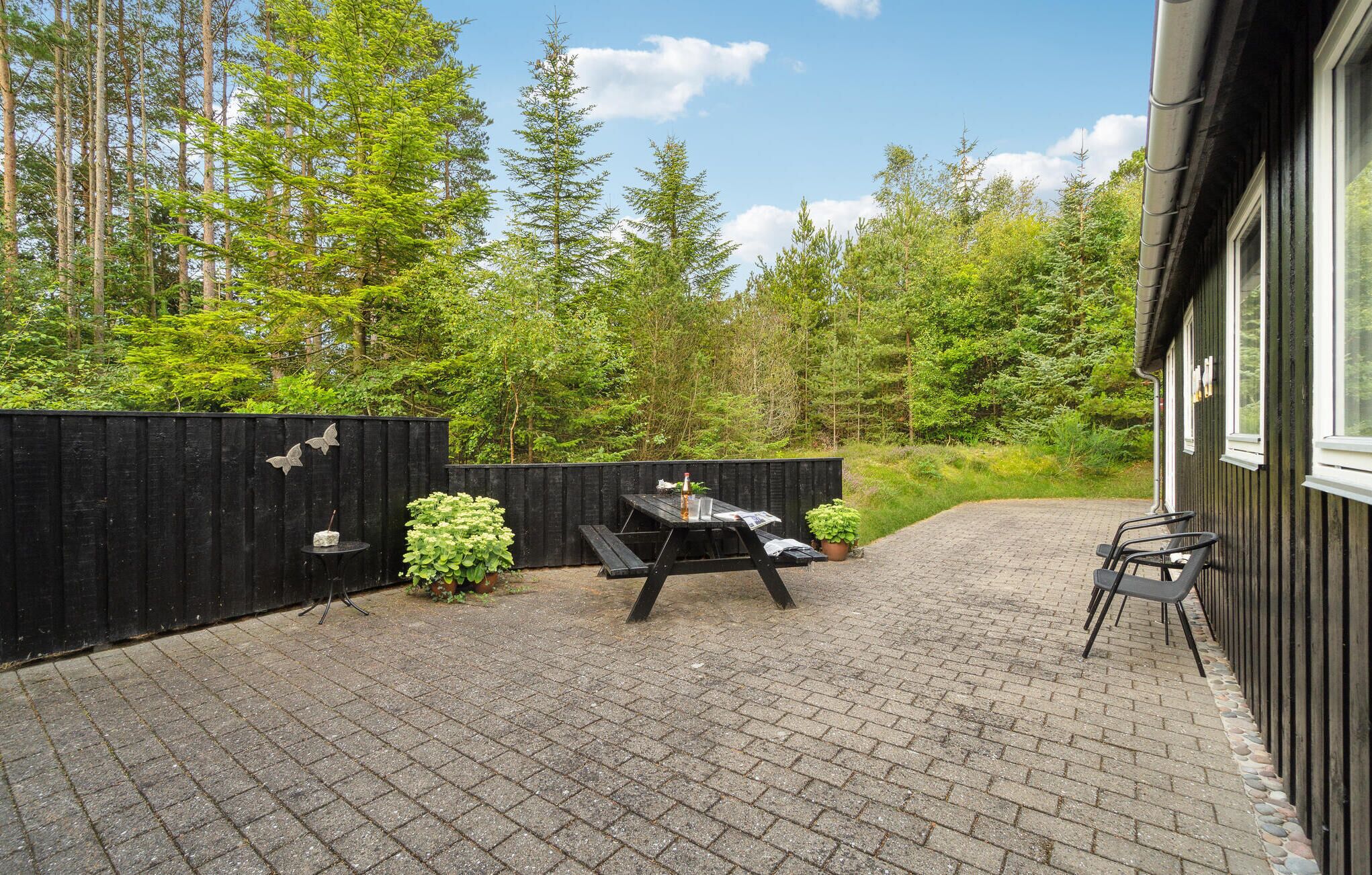 Un espace patio aménagé avec une table de pique-nique et des chaises, entouré d’une clôture en bois et d’une végétation luxuriante.