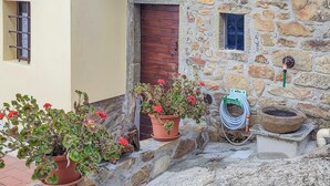 A stone building with a wooden door and a small window. There are potted plants with red flowers and a hose on the ground. - Lovely home in Marliana with WiFi (Marliana)