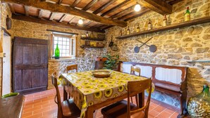 A rustic dining area with a stone wall, wooden beams, and a table set with a sunflower tablecloth. - Lovely home in Marliana with WiFi (Marliana)