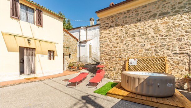A courtyard with a stone wall, a hot tub, and red lounge chairs. - Lovely home in Marliana with WiFi (Marliana)