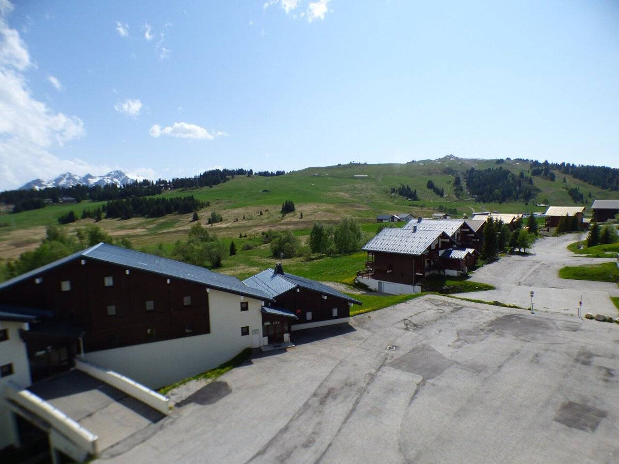 A rural setting with a row of wooden houses, a paved road, and a hilly landscape with mountains in the background.