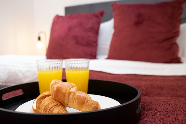 A breakfast tray with croissants and orange juice on a bed with red pillows.