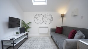 A modern living room with a grey sofa, a white coffee table, a flat-screen TV, a world map artwork, a floor lamp, and a potted plant.