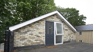 A small brick building with a dark door and a sliding glass window, a concrete roof, and a metal gate.