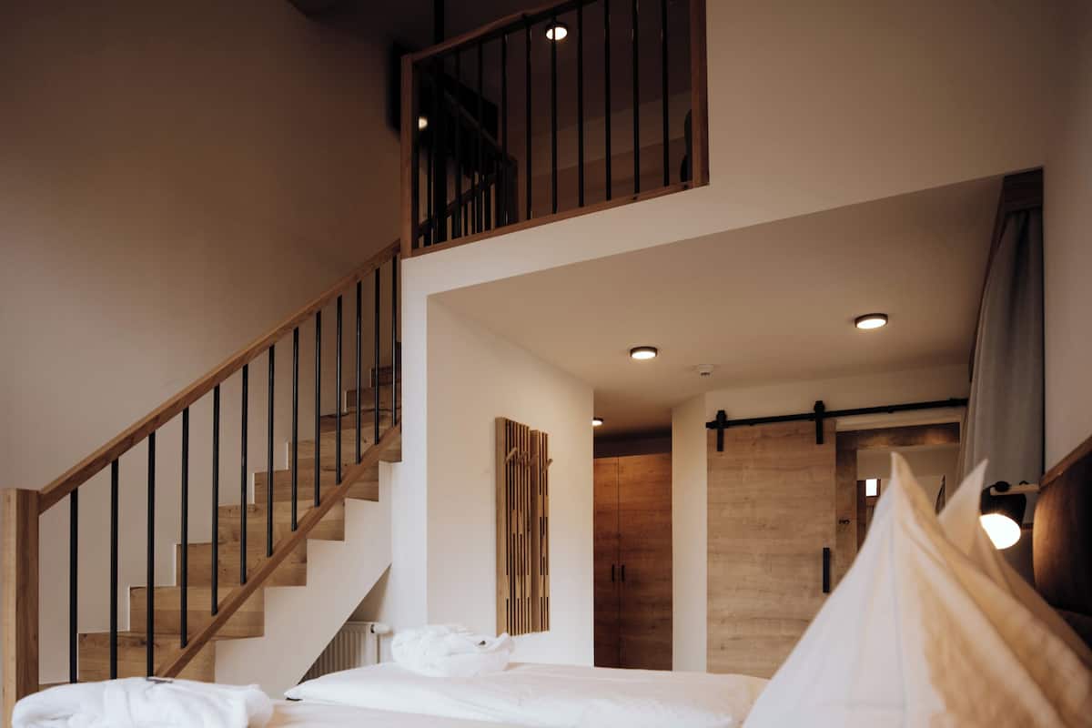 Un dormitorio con una cama grande, una escalera de madera y vistas al salón.