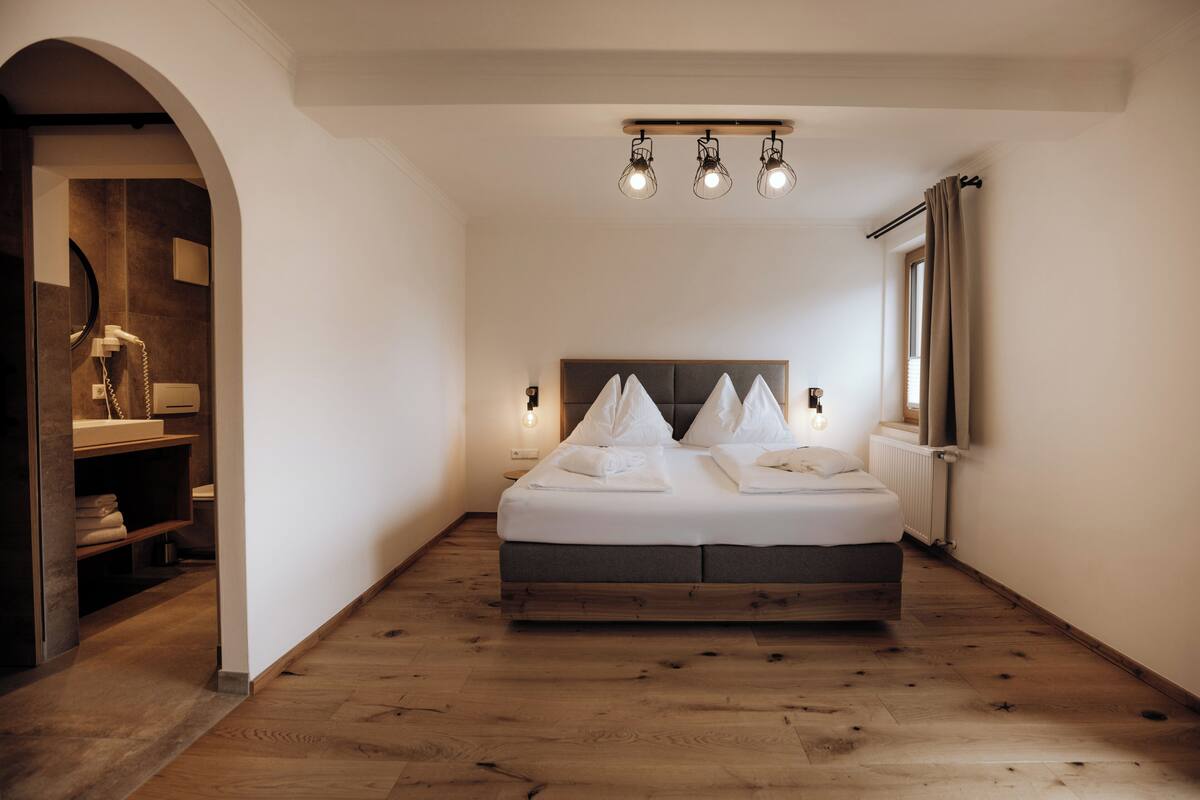 Un dormitorio con una cama grande, suelo de madera, armario empotrado y ventana con cortinas.