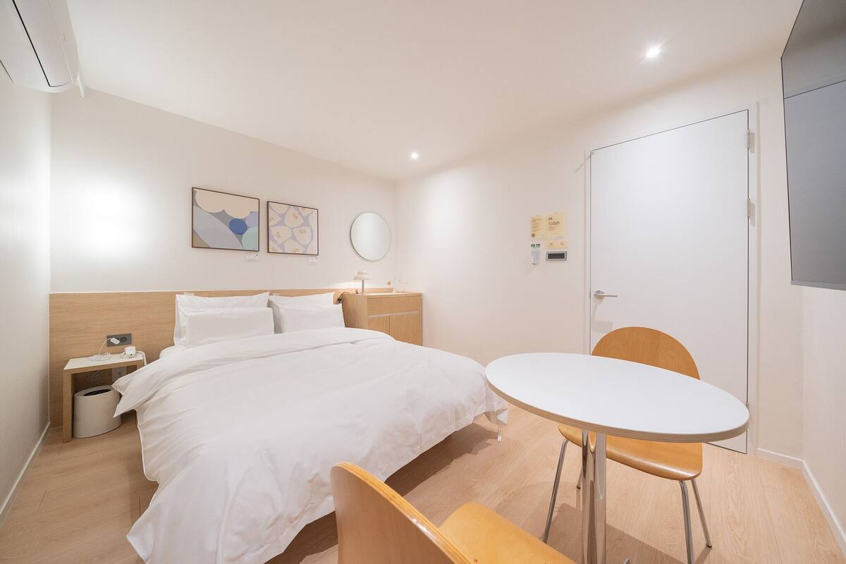 Habitación de hotel con cama, mesita de noche, silla, mesa redonda y una obra de arte en la pared.