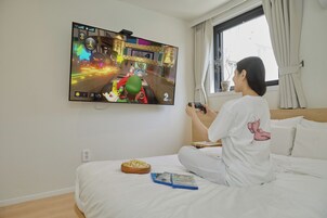 Una persona jugando un videojuego en la televisión, en una habitación con cama, un cuenco de palomitas de maíz y una ventana con cortinas.