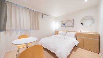 Habitación de hotel con cama, espejo redondo, una pequeña mesa con dos sillas y un armario de madera.