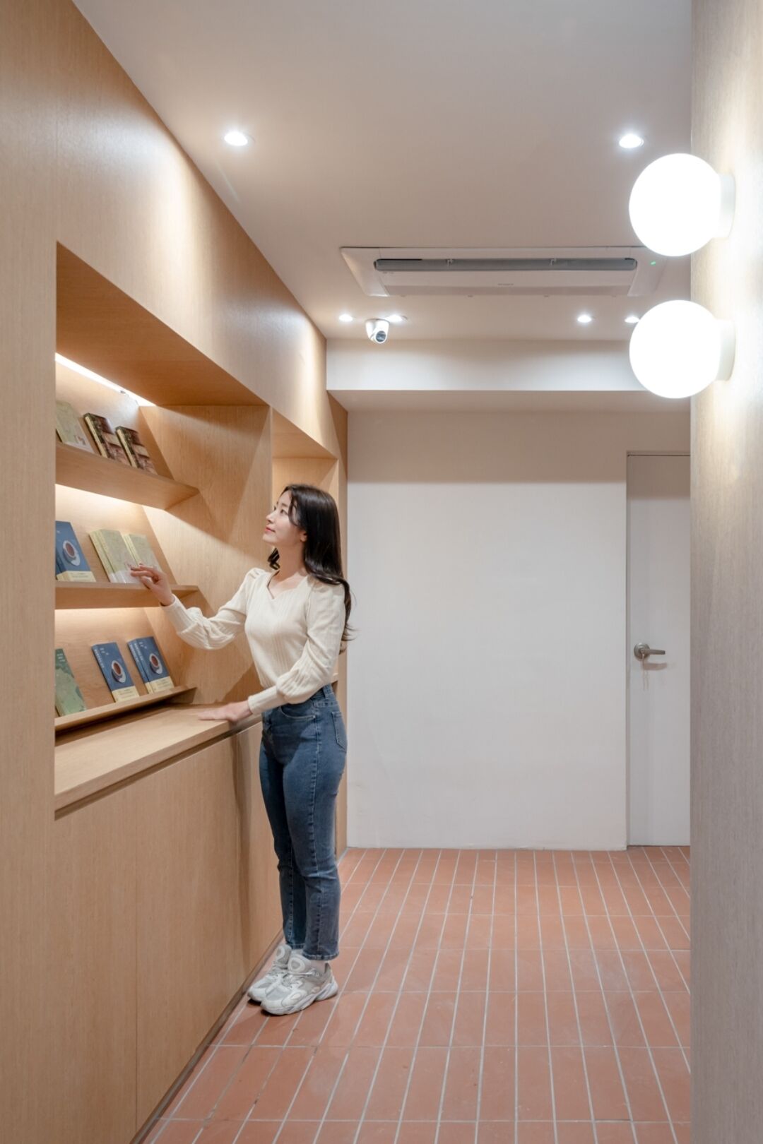 Una mujer parada en un pasillo con estanterías de madera que muestran libros y cuadros enmarcados.