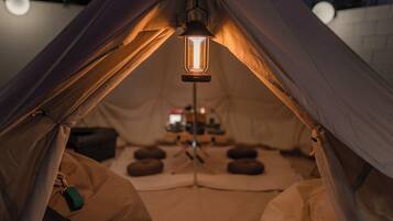 Een tent van binnen, met een hanglamp, een driepoot en een tafel met spullen erop.