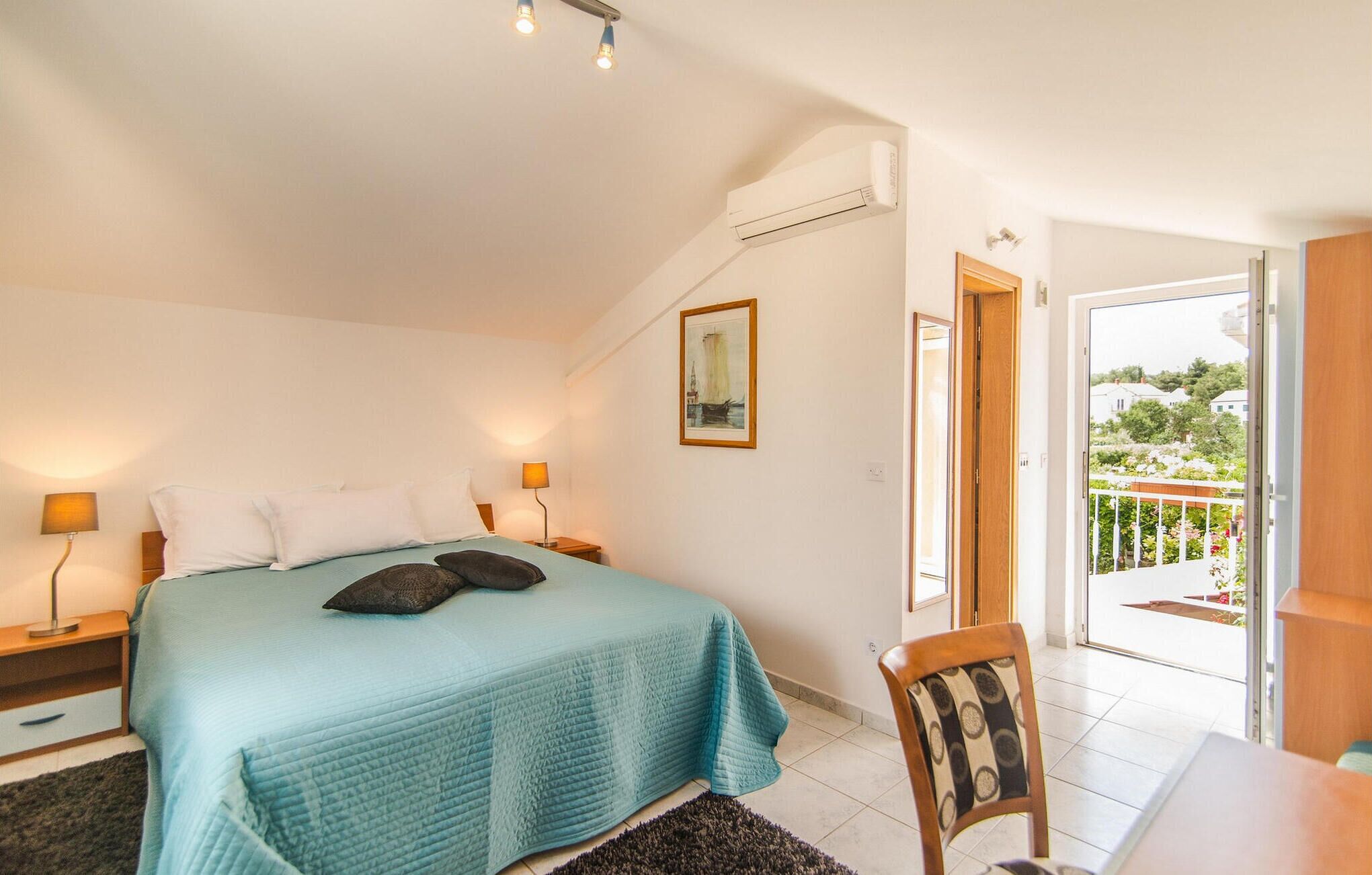 A bedroom with a bed, bedside lamps, a painting, and a view of the outside.