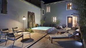 Une terrasse extérieure bien éclairée, dotée d’une piscine, de chaises longues et d’un espace repas.