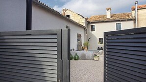 Une cour avec un chemin de gravier, un bâtiment blanc doté d’un toit en tuiles et un portail gris.